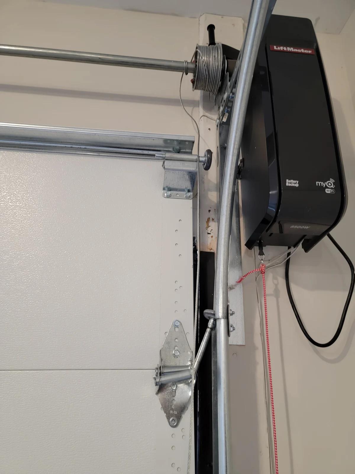 Wall-mounted garage door opener beside the door shaft and cable drum.