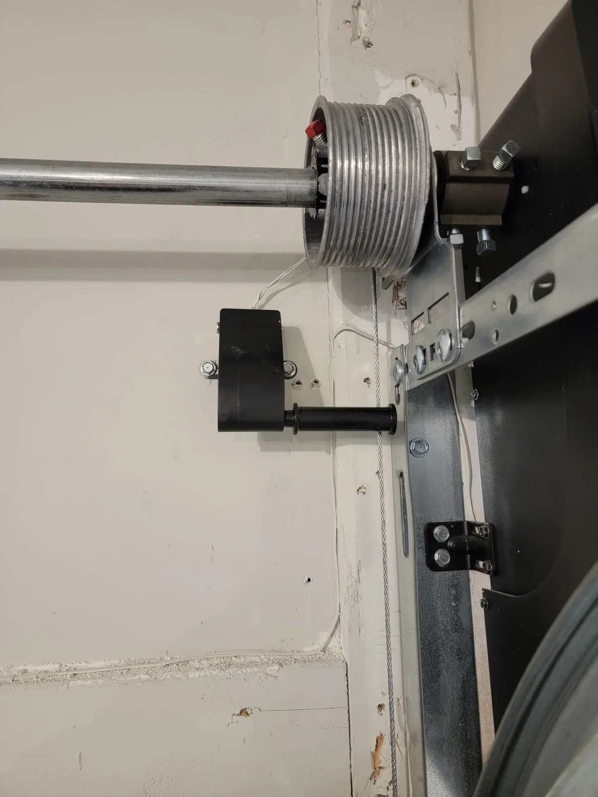 Garage door cable drum, vertical lift cable and the adjacent cable-tension monitor.