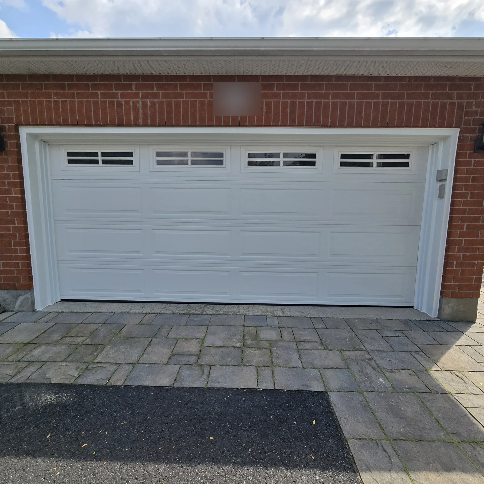 White double garage door with a white capped surround against red brick.