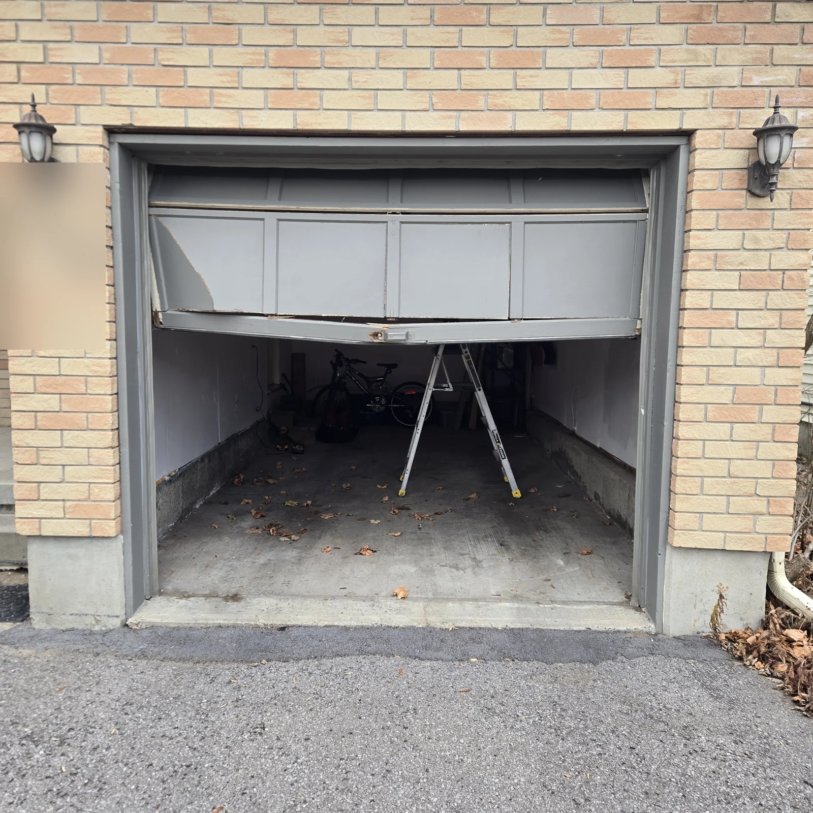 Buckled white garage door at the same brick opening shown in the replacement photograph.