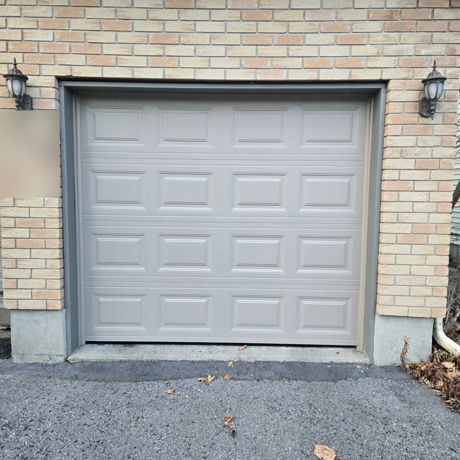 Raised-panel replacement door in a pale neutral finish, between two black lanterns.
