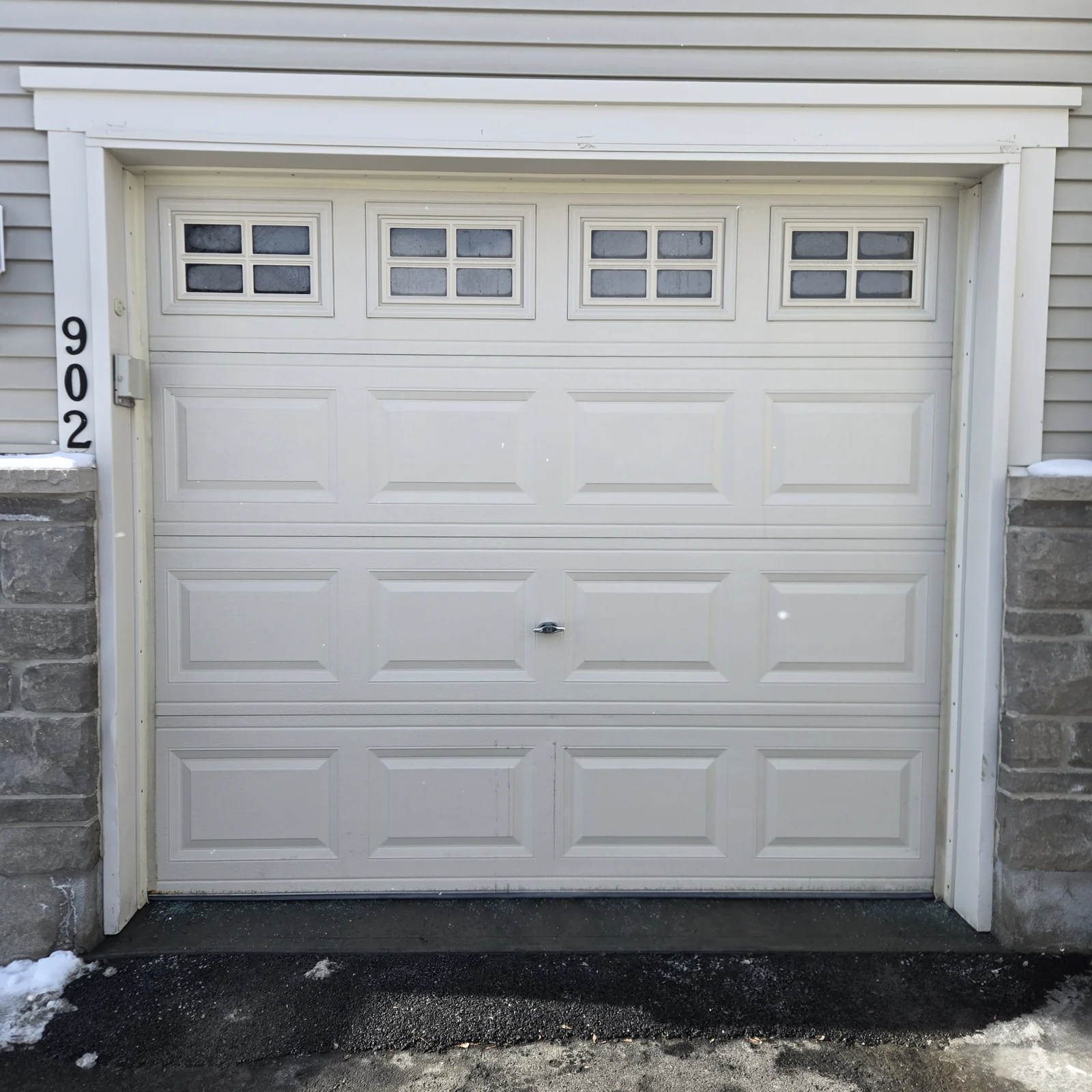 Existing garage door with window inserts, in a pale neutral finish, before replacement.