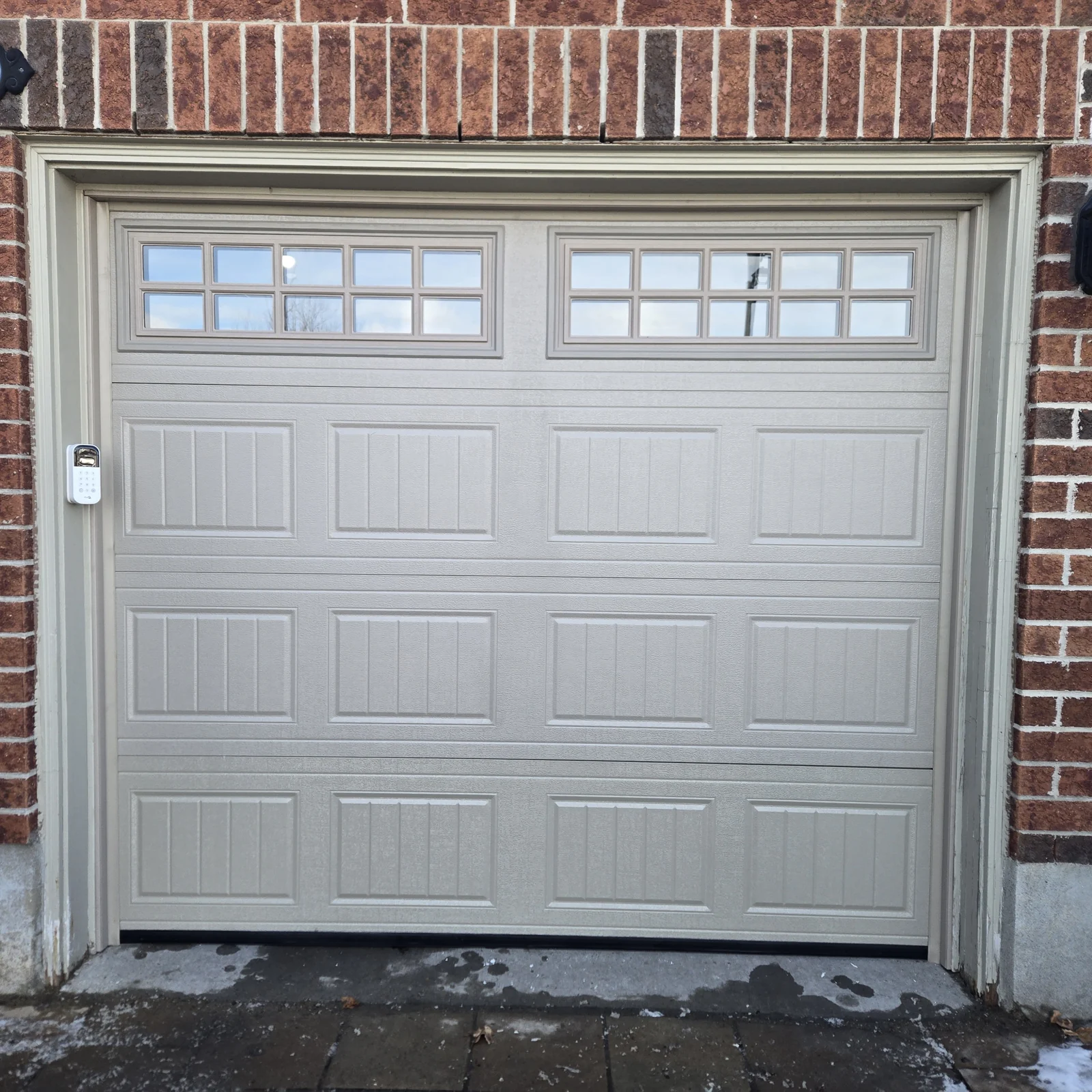 Raised-panel garage door with two rows of windows in a red brick opening.
