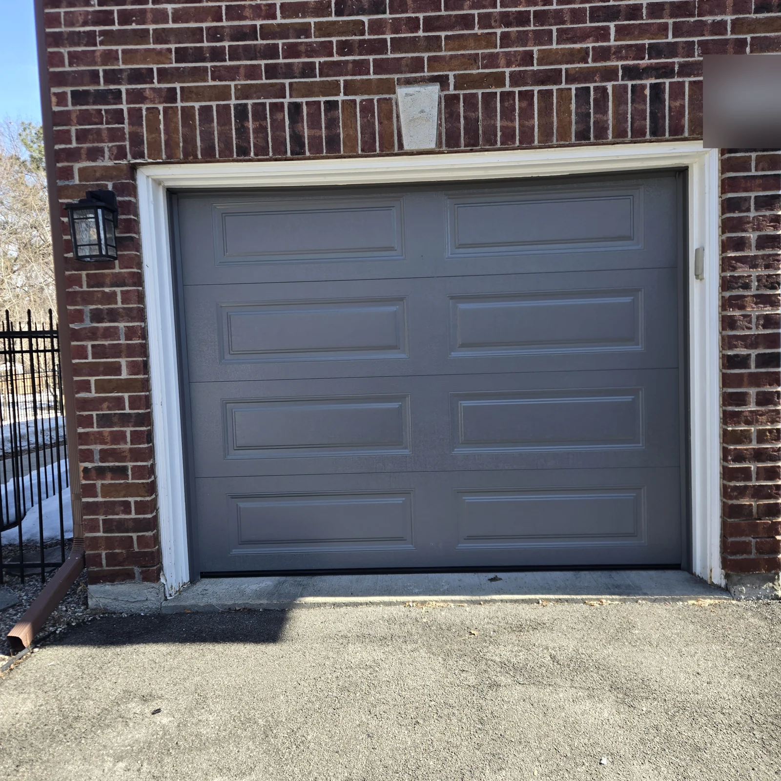 Grey raised-panel single garage door against red brick.