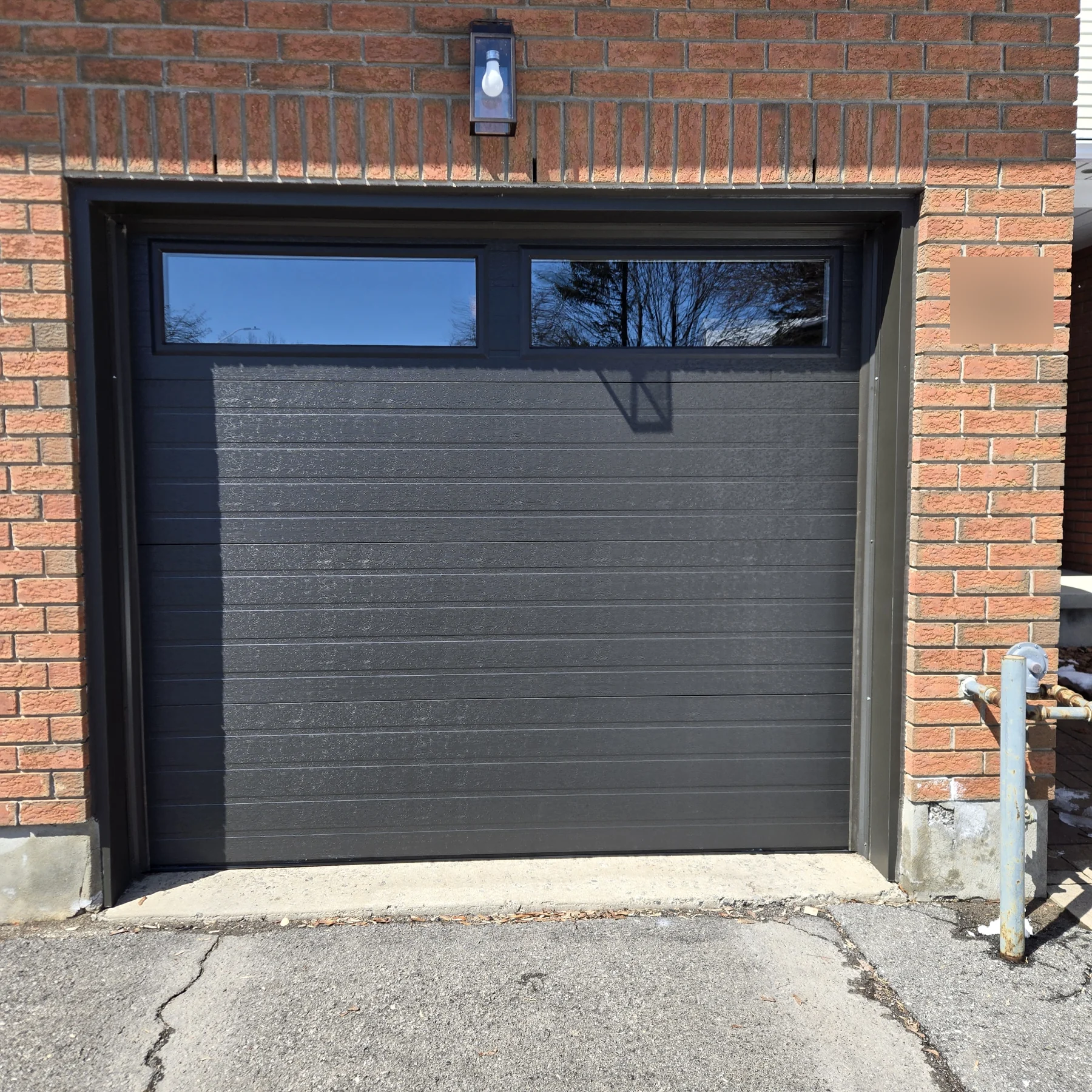 Black horizontal-panel garage door with a row of top windows in a red brick opening.