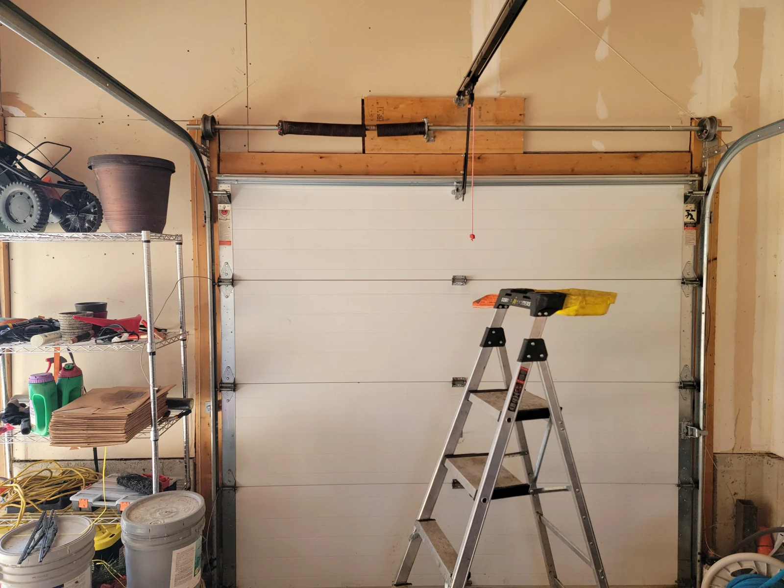 Before: Broken torsion spring above a white sectional garage door.