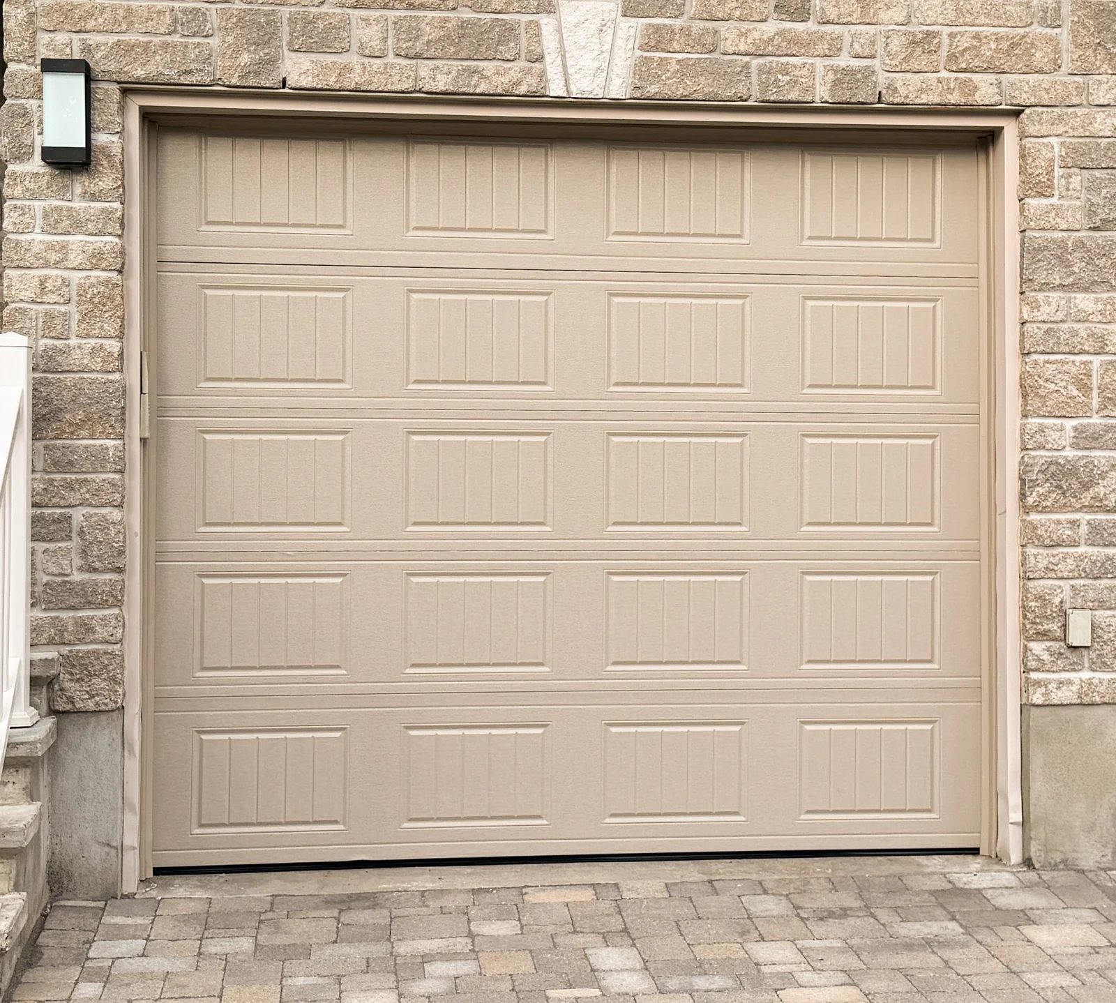 Raised-panel garage door in a warm neutral finish, framed by brick.