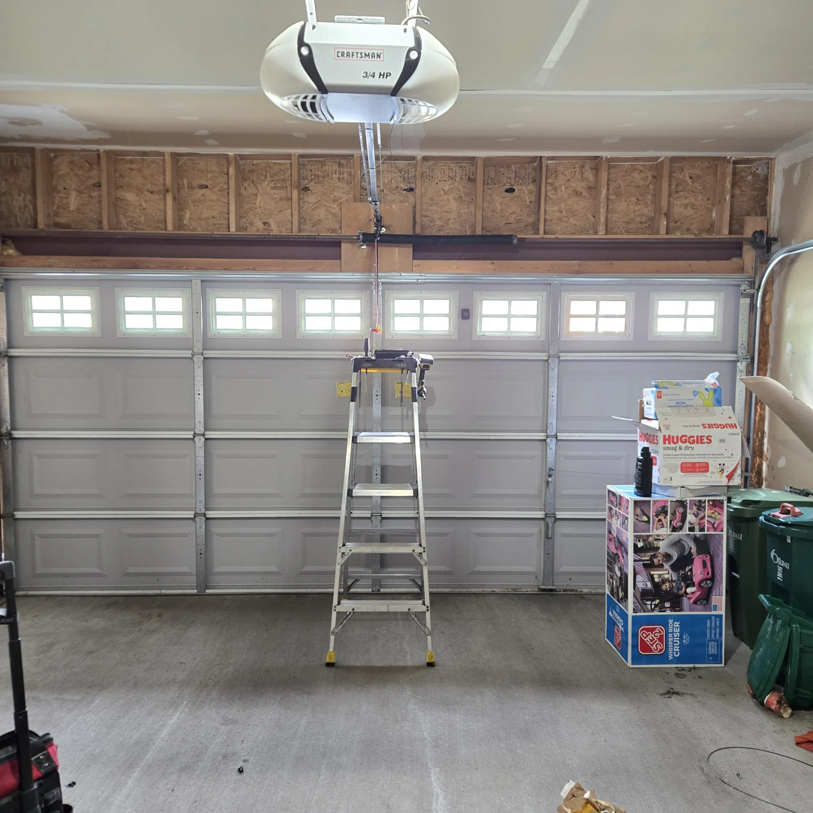 Displaced garage door closed and secured again in an unfinished garage, with a ladder still standing in the opening.