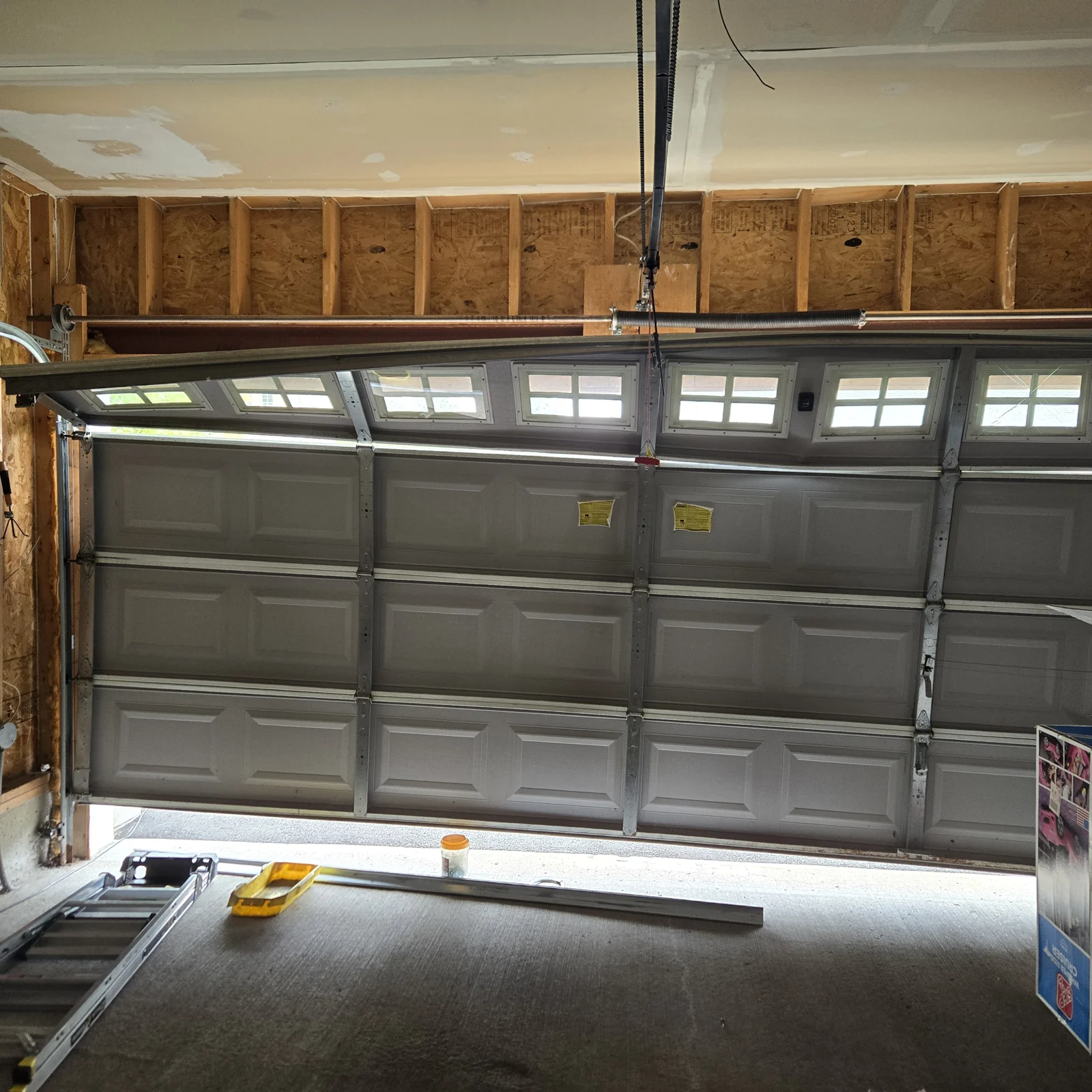 The same unfinished garage opening with the door closed and running straight after the repair.