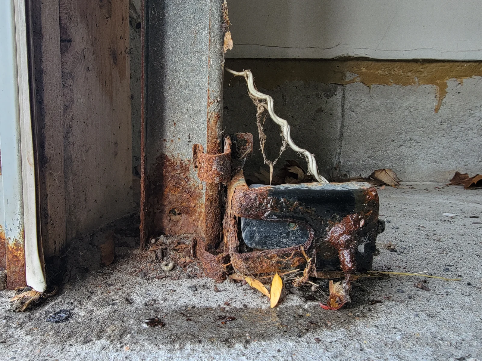 Heavily corroded garage-door safety photo-eye and floor-level bracket before replacement.