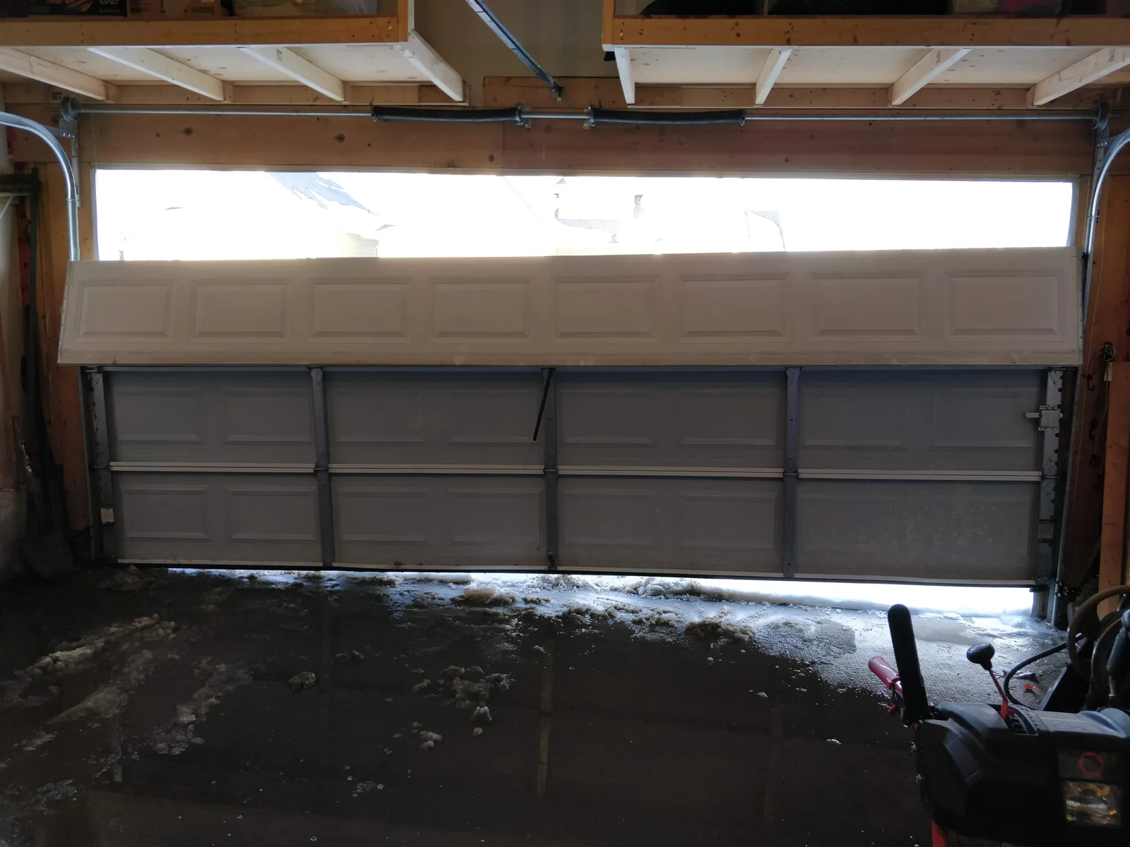 Skewed sectional garage door below a storage loft before realignment.
