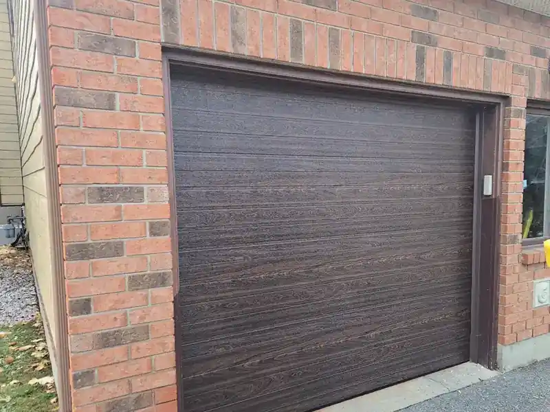 Modern dark woodgrain garage door in a brick opening.