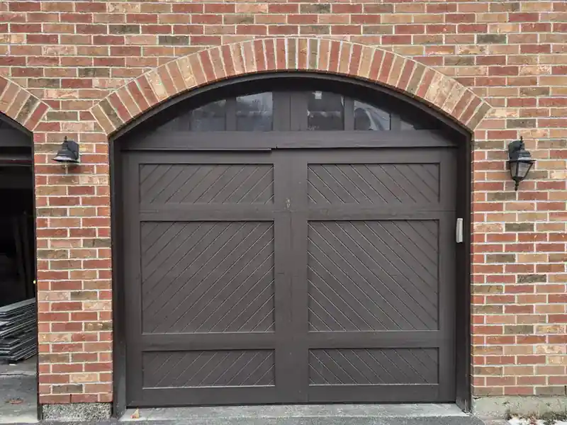 Dark carriage-style garage door beneath an arched brick opening.