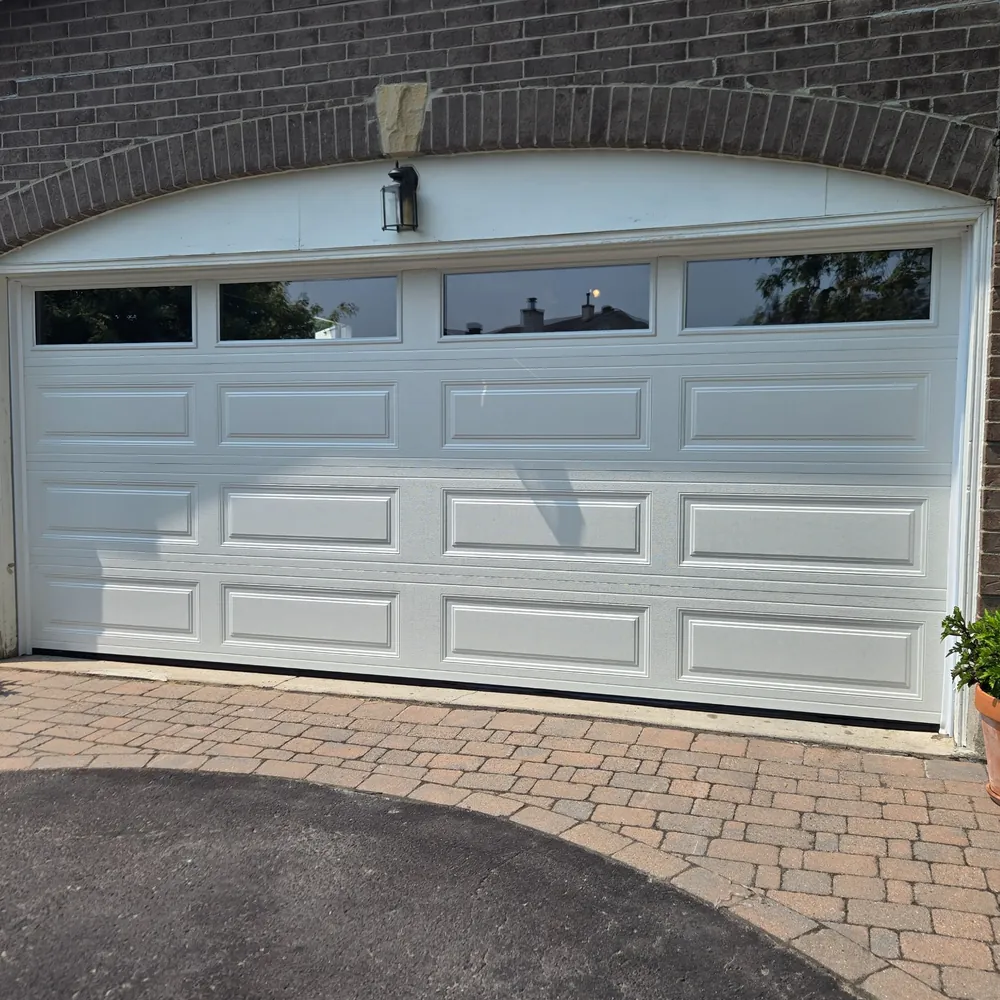 White double garage door with raised panels and four rectangular top windows beneath a brick arch.
