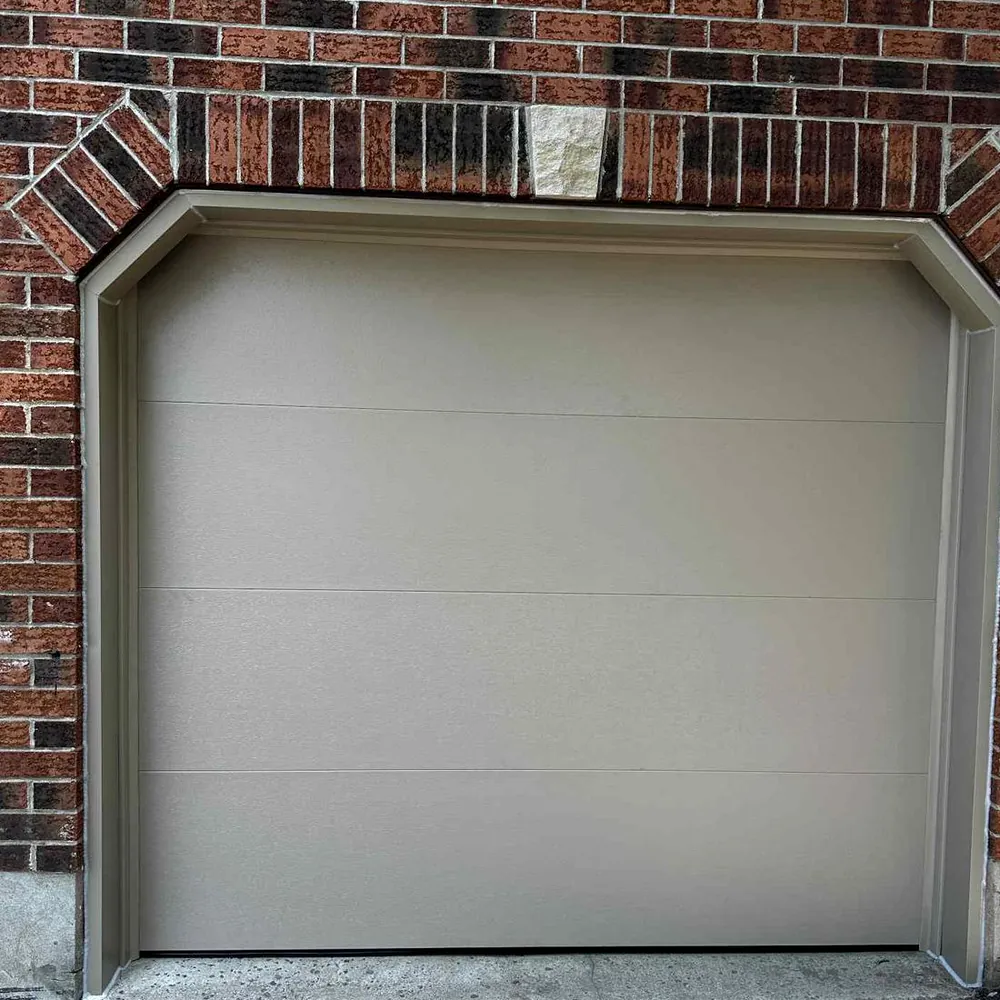 Minimal flush garage door in a light neutral finish inside a chamfered brick opening.