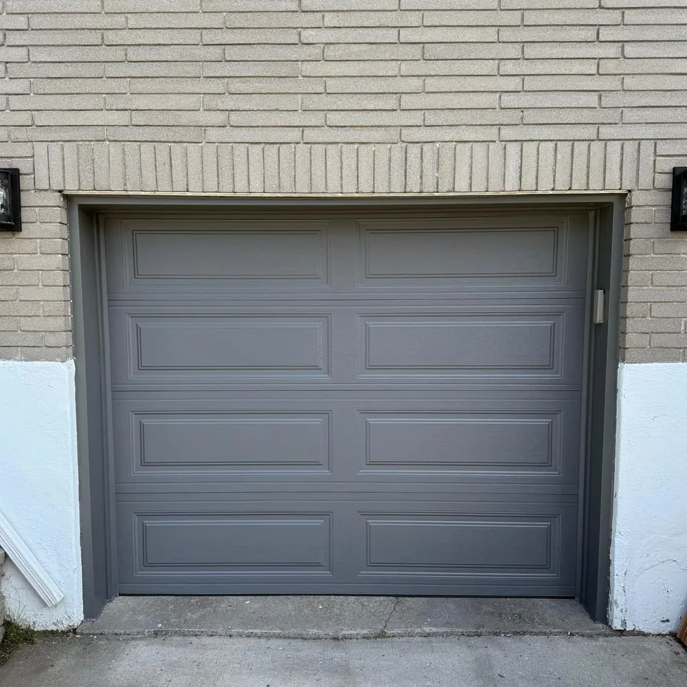 Charcoal raised-panel single garage door against pale brick.