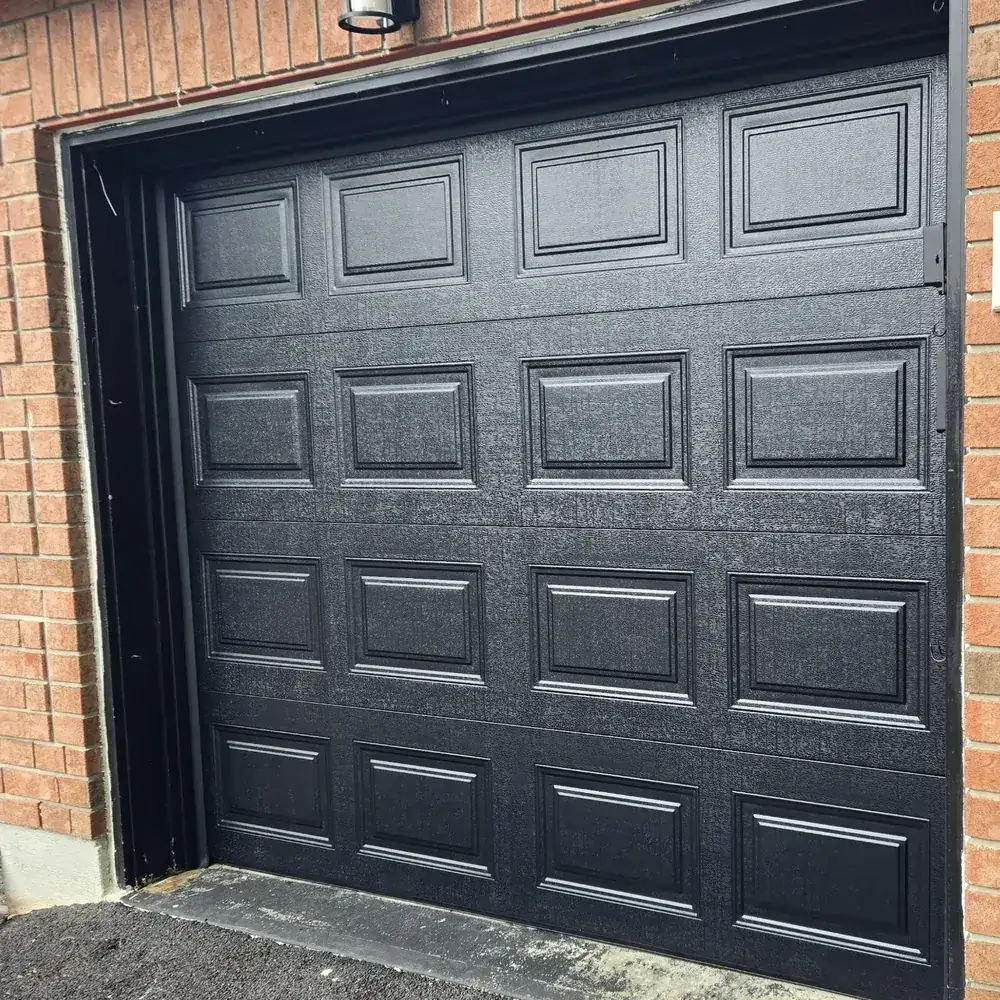 Black raised-panel single garage door framed by red brick.