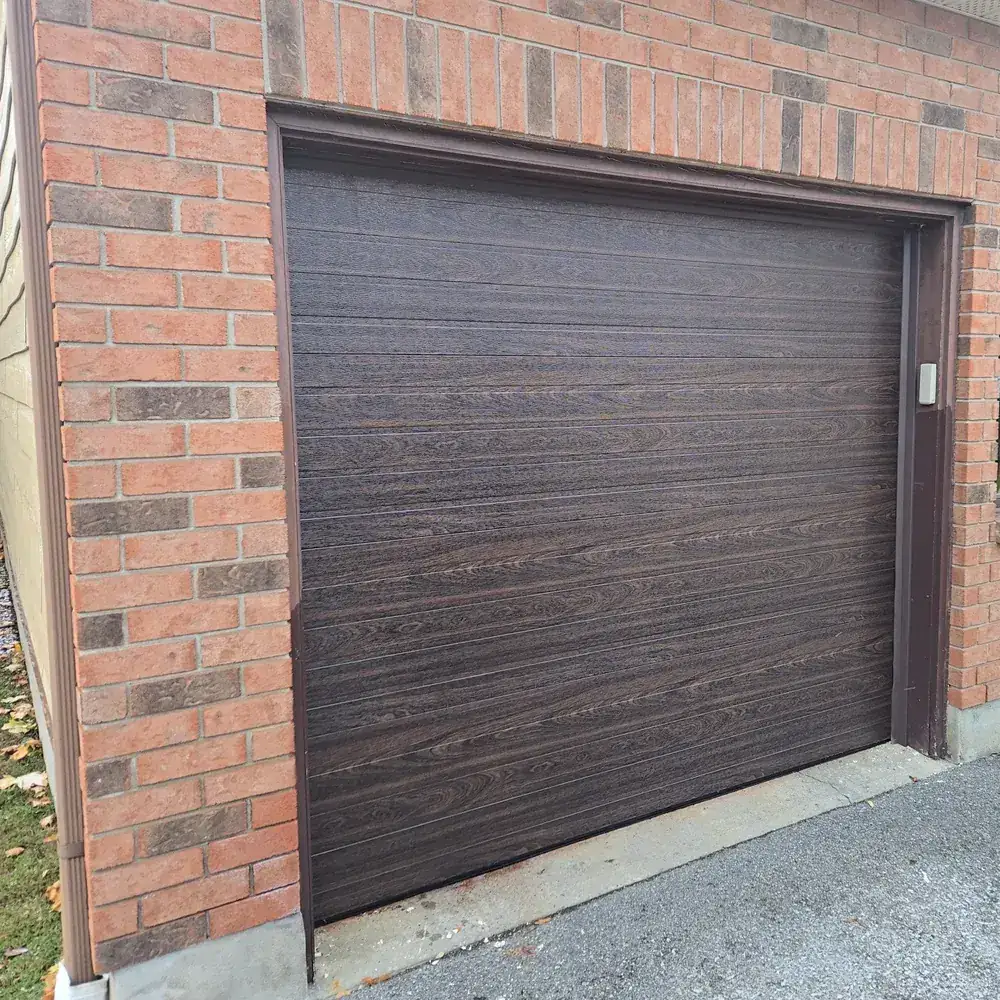 Dark woodgrain flush-panel garage door set in a red brick opening.